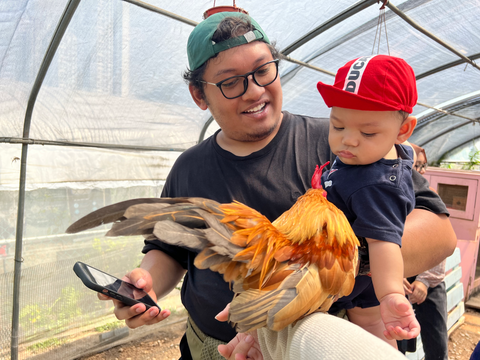 A father and young son meeting a chicken together at a City Sprouts Family Day corporate bonding event.