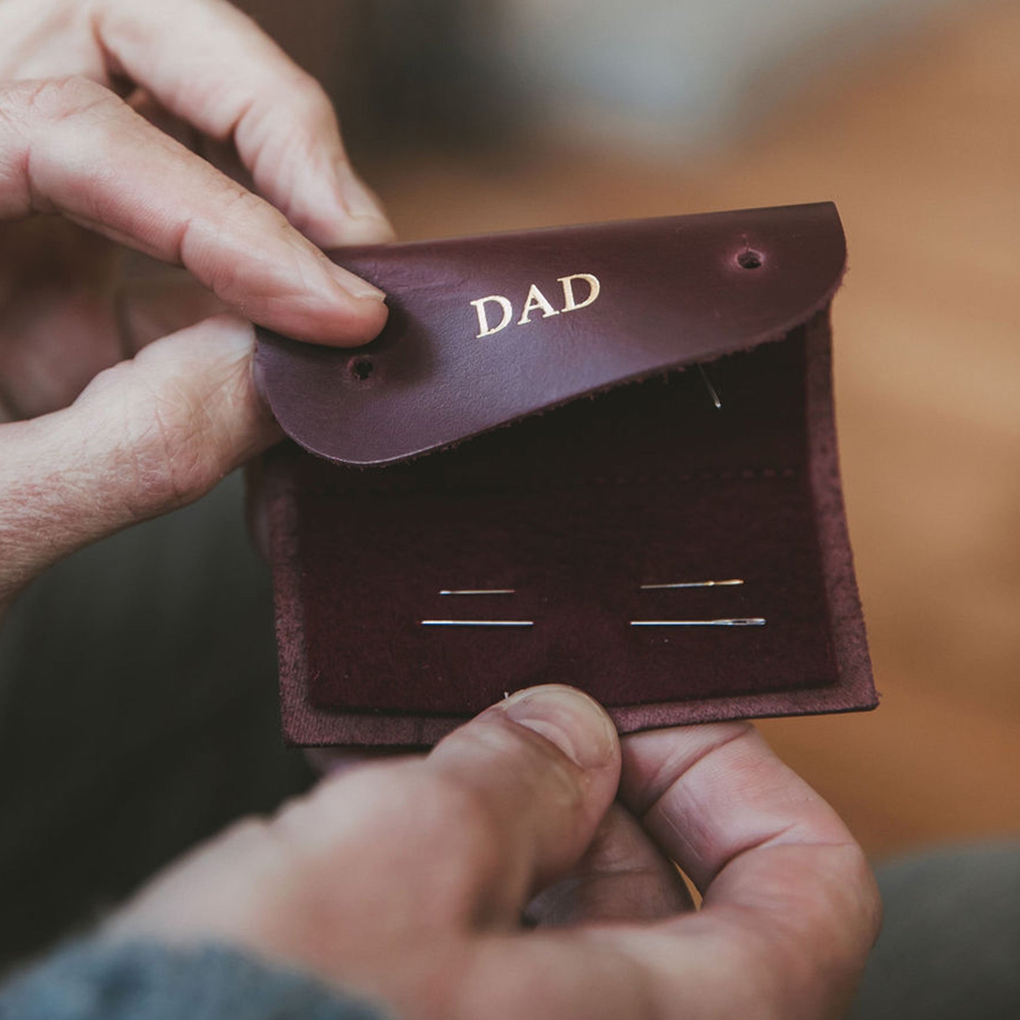 Man holds brown leather sewing needle case with Dad personalised on it.