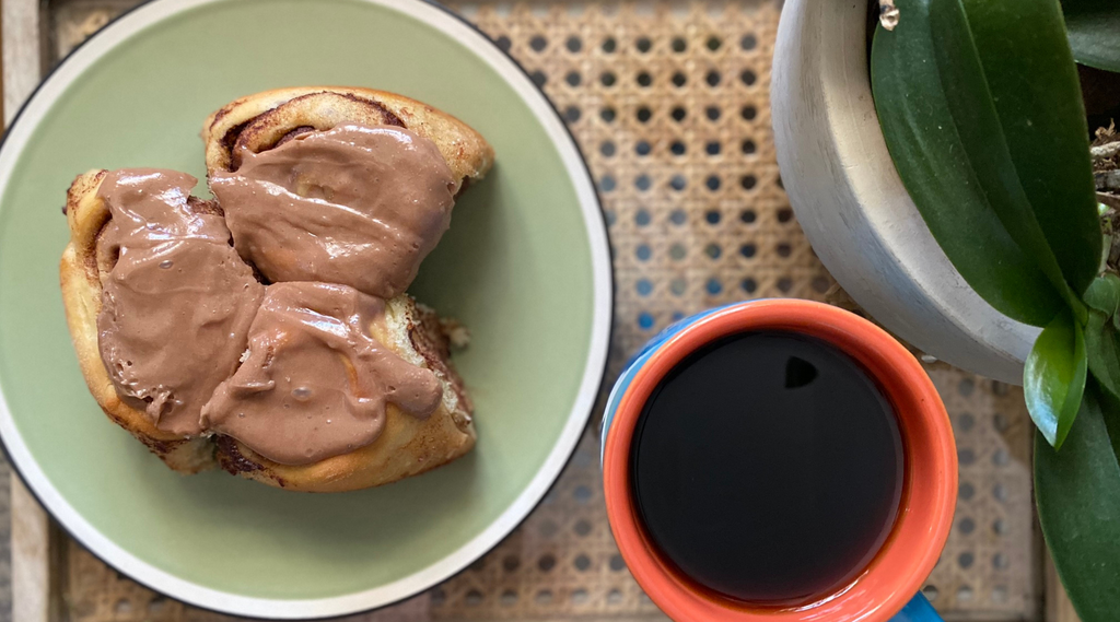 a plate of irish cream rolls sits next to a black cup of coffee and plant