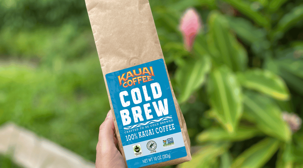 kauai coffee cold brew bag is held outside. A pink tropical flower is visible in the background