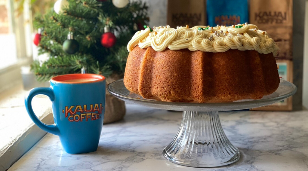 Kauai Coffee eggnog latte bundt cake sitting on a cake stand in front of a small decorated tree and holiday coffee bags