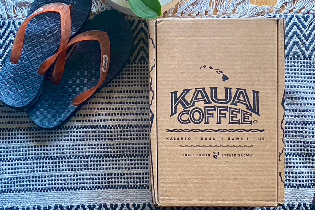 kauai coffee shipping box sits on a rug outside a home with a pair of flip flops