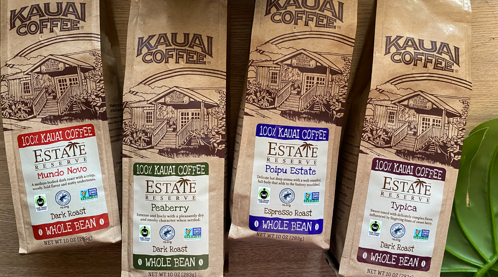 four bags of kauai coffee estate reserve lay on a wooden table surface. They have colorful labels that are aligned in rainbow order