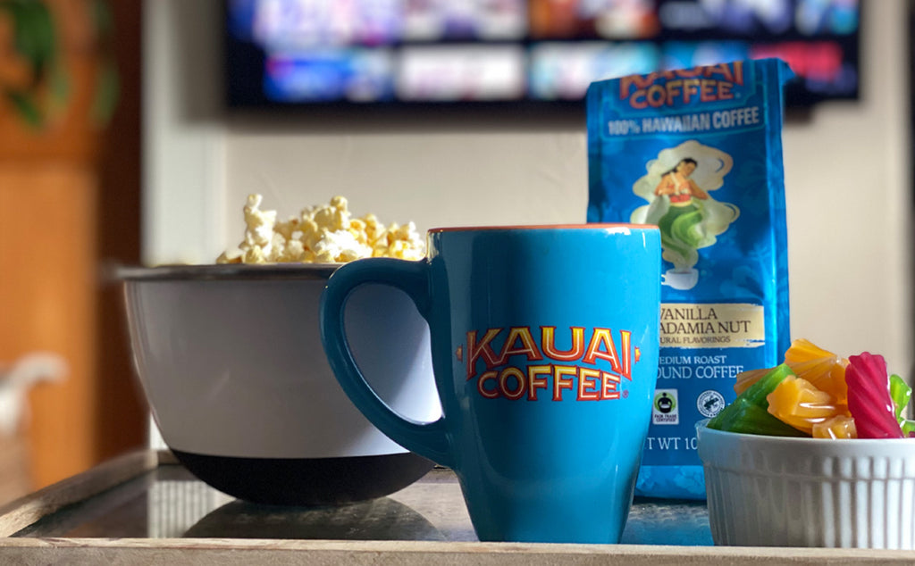 a kauai coffee mug and bag of vanilla macadamia nut coffee sit on a small tv table. A wall mounted tv is visible in the background