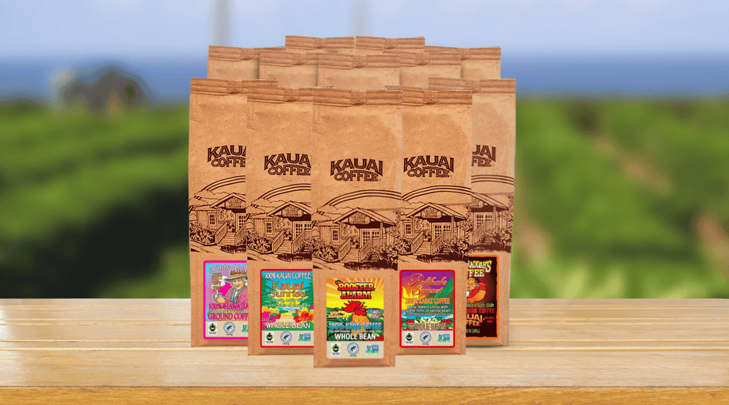 kauai coffee ohana collection bags sit on a wood surface with a blurred image of the farm in the background