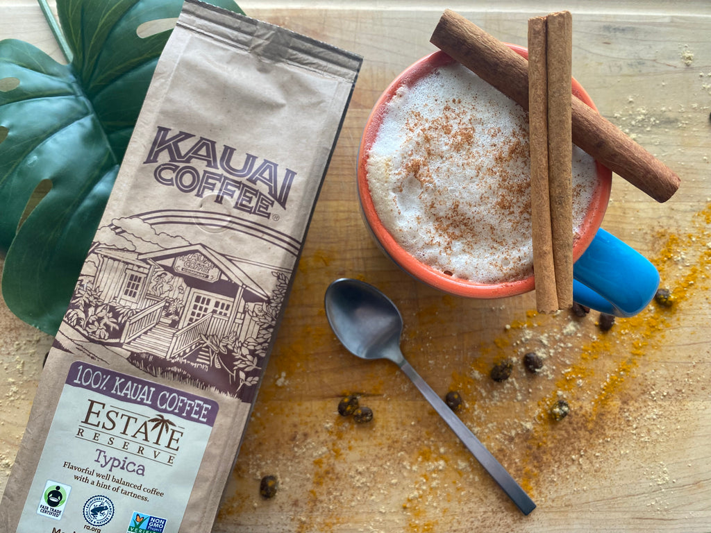 kauai coffee spiced latte and bag of typica coffee sit on a wooden board with a dusting of spices and cinnamon sticks