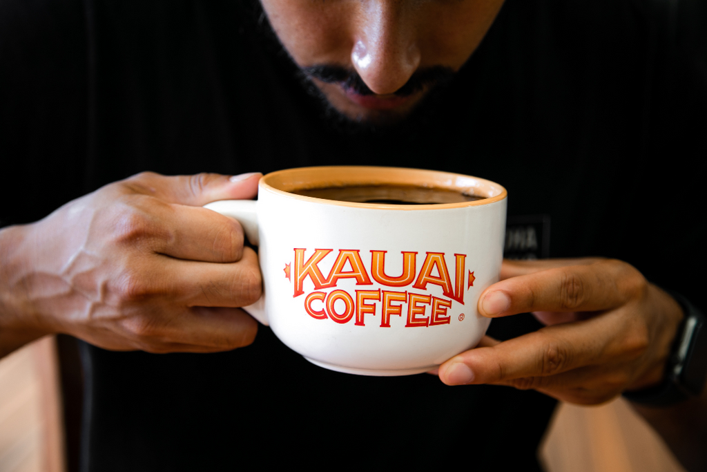 a customer sips kauai coffee from a large white mug with the kauai coffee logo on it