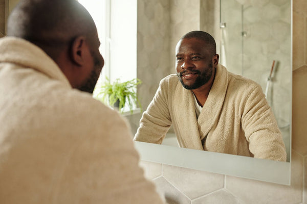 black man in robe looking in bathroom mirror