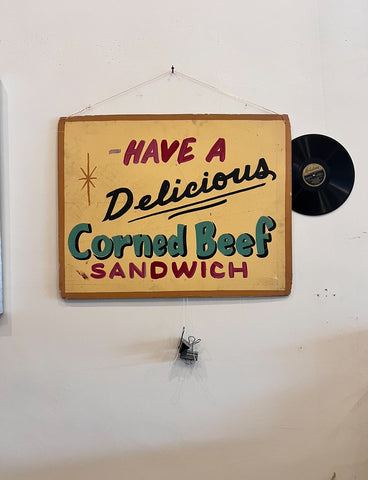 Vintage hand painted sign that reads "have a delicious corned beef sandwich"