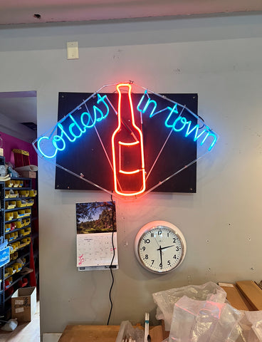 Original neon sign with blue letters that say "coldest in town" and a red beer bottle in the middle