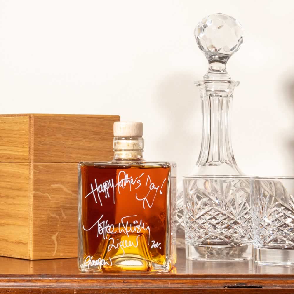 Cube bottle of Spiced Rum in the forefront, oak gift box behind and crystal glass and decanter to the right