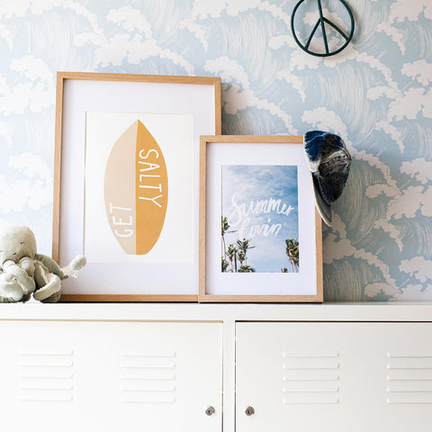 Children's coastal themed room with surfboard and palm tree art styled upon a white cabinet against blue wave wallpaper