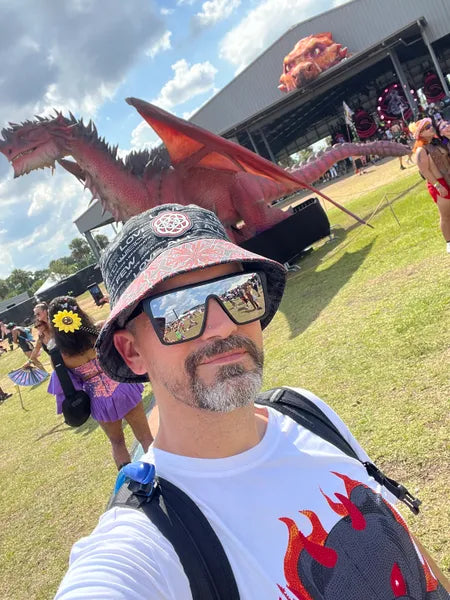 Man in a hat at a festival with a dragon sculpture.