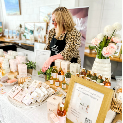 Image is of Lady Daa Doo standing behind a market stall with the entire product range on the table