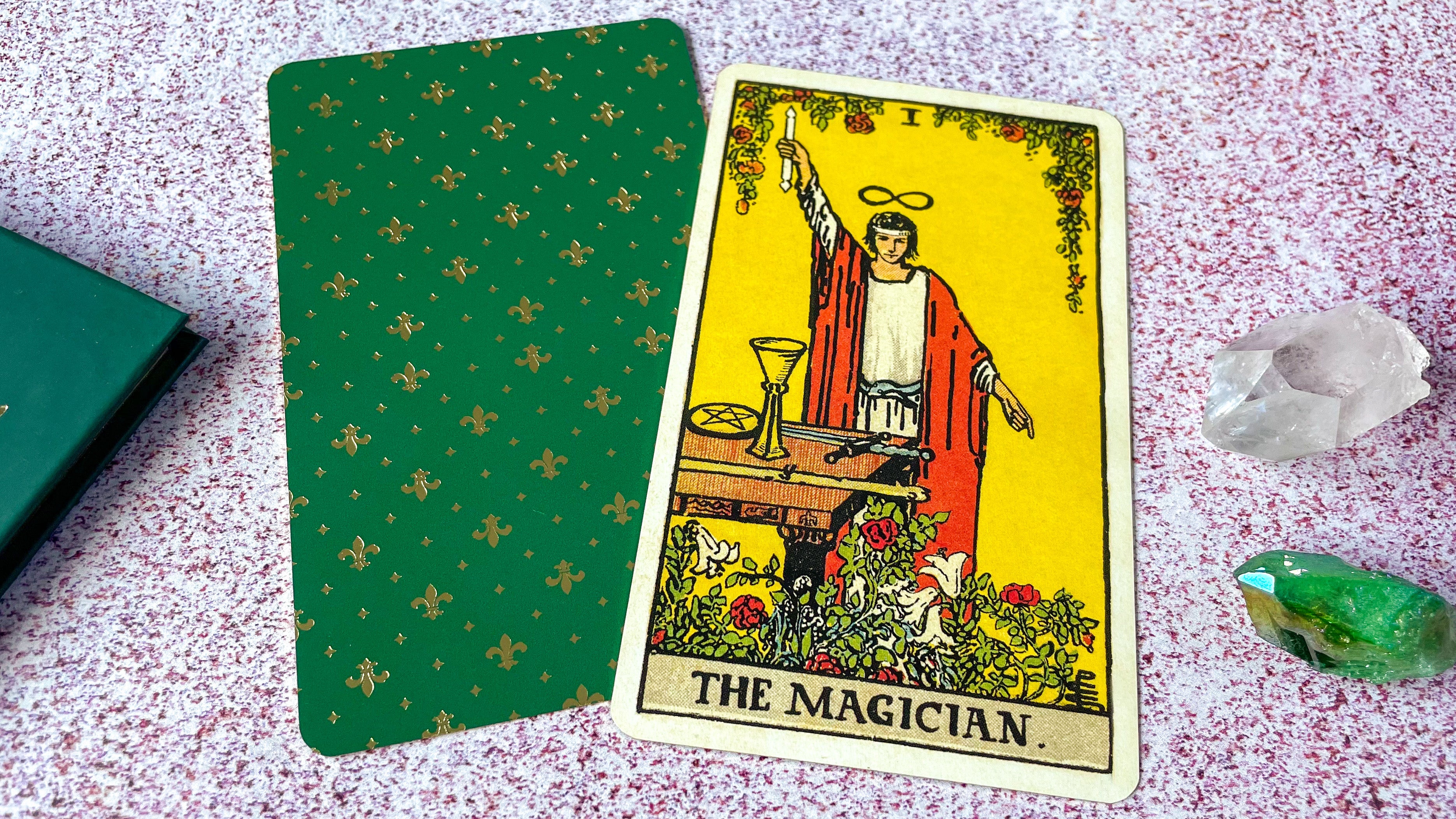 The traditional Rider Waite Magician tarot card laying flat on top of a green card back.