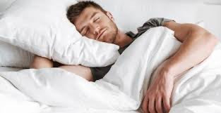 Man sleeping with smile on his face on bed with white sheets.