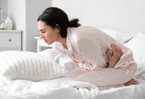 Woman on her bed crouched over in pain with a look of distress on her face.