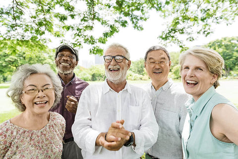 5 elderly people smiling with a tree behind them outside.