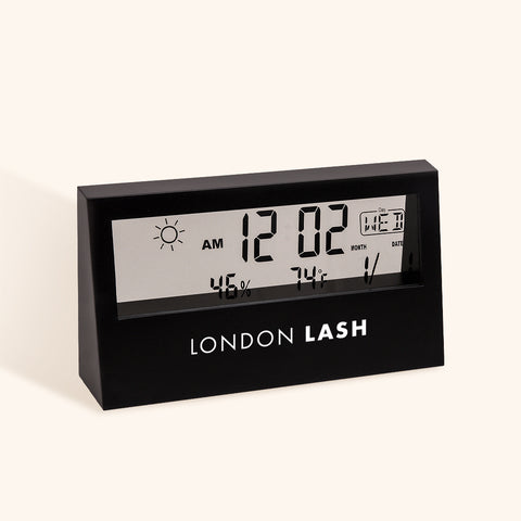 A photo of a hygrometer which is used to track humidity and temperature in a lash tech's work area. This one also displays the time and date, is made from matte black plastic and has a transparent screen | London Lash Australia