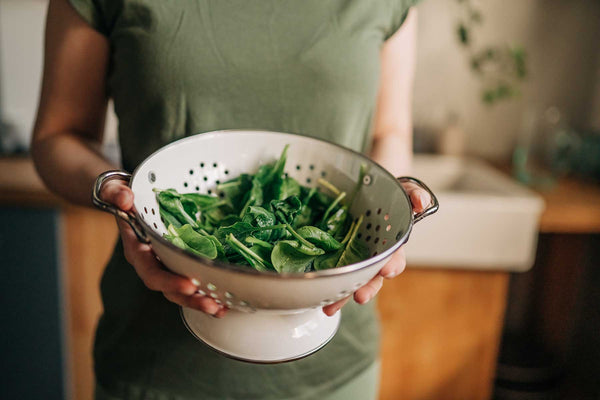 Woman holding a colander of bright green spinach