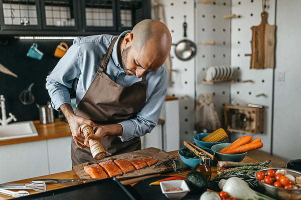 Man in an apron seasons salmon with pepper before cooking