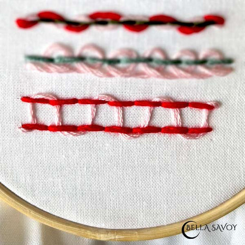 2 horizontal parallel back stitches in red. Needle with pink thread sliding up 1st stitch in both rows