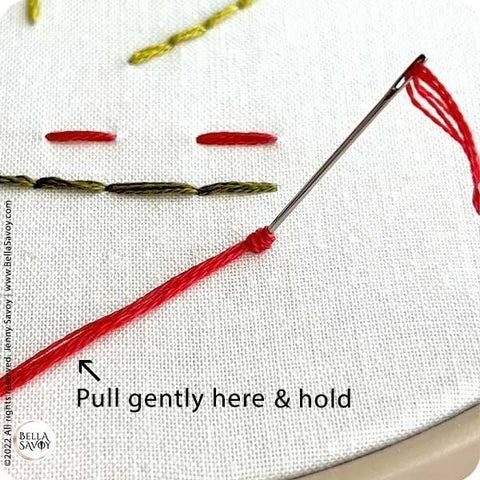needle pushed halfway into fabric with thread wrapped around it