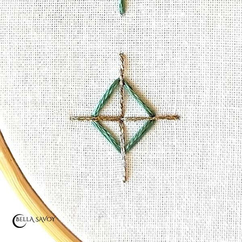 teal diamond stitched shape with a rose gold cross over it