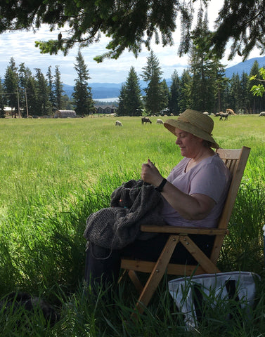 Woman sitting under tree knitting in sheep pasture