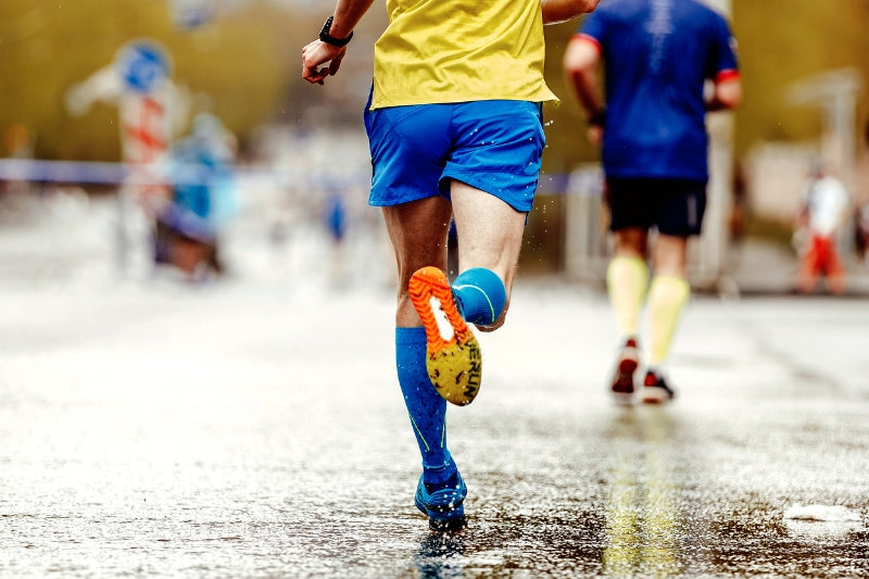 Man wearing blue compression socks running on road outdoors