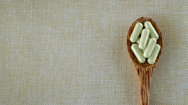 A close-up of a wooden spoon filled with pale green supplement capsules resting on a neutral woven fabric, illustrating quercetin in capsule form.