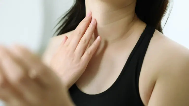 A woman gently touching her neck and jawline in front of a mirror, illustrating the skincare and antioxidant benefits of glutathione for skin health, detoxification, and longevity.