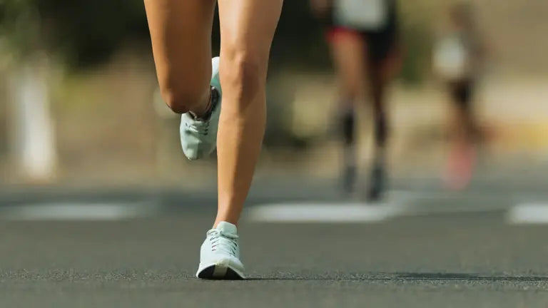 Close-up of a runner’s legs mid-stride on a sunlit road during a race, symbolizing the endurance and energy benefits of taking the right NMN dosage.
