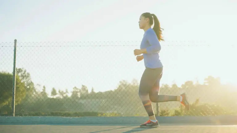 Woman jogging along a sunlit path beside a chain-link fence at sunrise, symbolizing the energy and vitality benefits of NAD boosters.