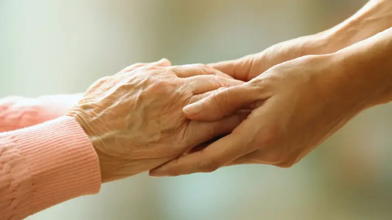A close-up of a younger person’s hands gently holding the aged, wrinkled hands of an older adult, symbolizing the relationship between aging and physical activity decline.