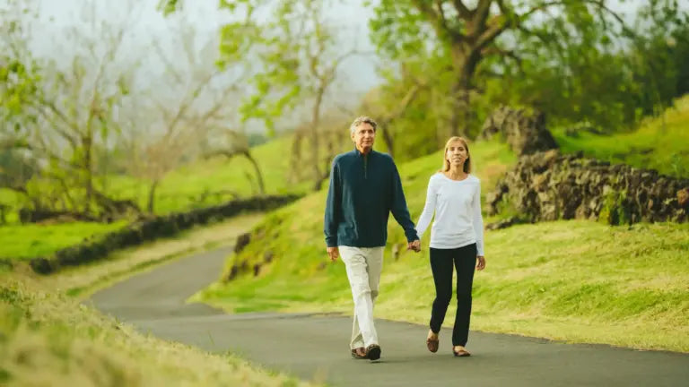 An older couple walking hand-in-hand along a tree-lined path in a green park, symbolizing active aging and the vitality promoted by spermidine supplementation.