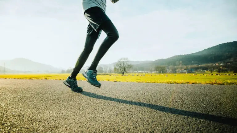 Close-up of a runner’s legs in motion on a sunlit country road, symbolizing the endurance and vitality benefits of calcium alpha-ketoglutarate supplementation.