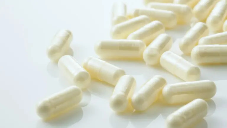 A scattering of white NMN supplement capsules on a clean white surface, illustrating one of natural sources of nicotinamide mononucleotide.