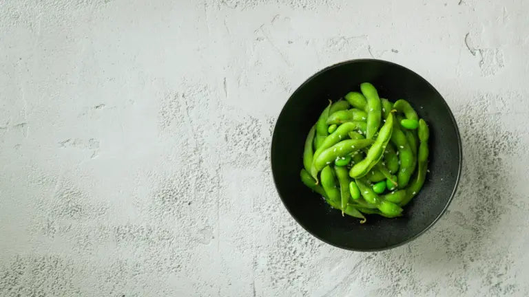 A black bowl filled with bright green edamame pods sprinkled with sea salt, highlighting a natural source of NMN.