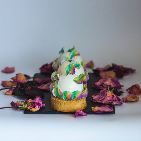 Individual cakes with rainbow-colored sugar petals and crushed floral decorations.