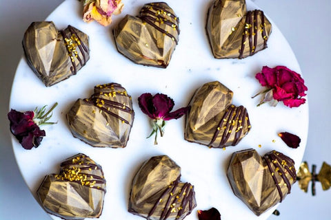 Chocolate heart candies brushed with edible gold dust and arranged with floral decorations.