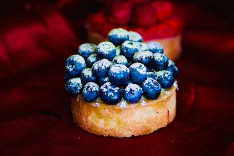 Image of one individual tart topped with blueberries, matcha powder, and powdered sugar.