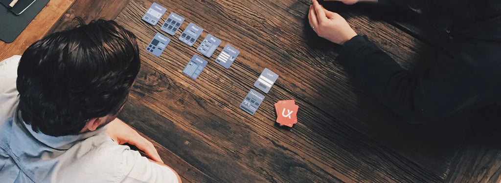 Two people sit at a table huddled over a set of website deck cards.