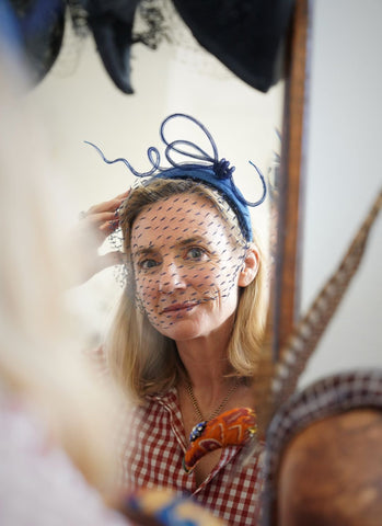 Portrait photo of Tara O'Callaghan, the Wiltshire milliner who makes hats for women and men for special occassions. She is wearing a netted headband and is looking in a mirror with hairbands all around