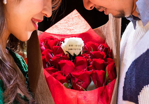 「世界一幸せな夫婦になろう」というメッセージの入ったバラの花束でプロポーズするカップル