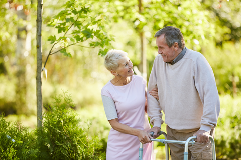 Older man using a walker to stroll outdoors with a smiling older lady.
