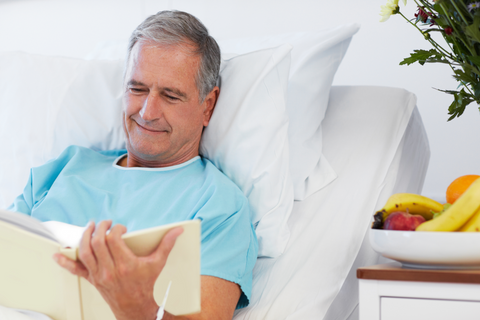 A man sits up in bed reading and recovering in comfort.