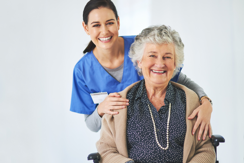 A happy caregiver stands behind a smiling older lady, who sits in a wheelchair. CapeAbilities provides specialist wheelchair sales, service and hire.