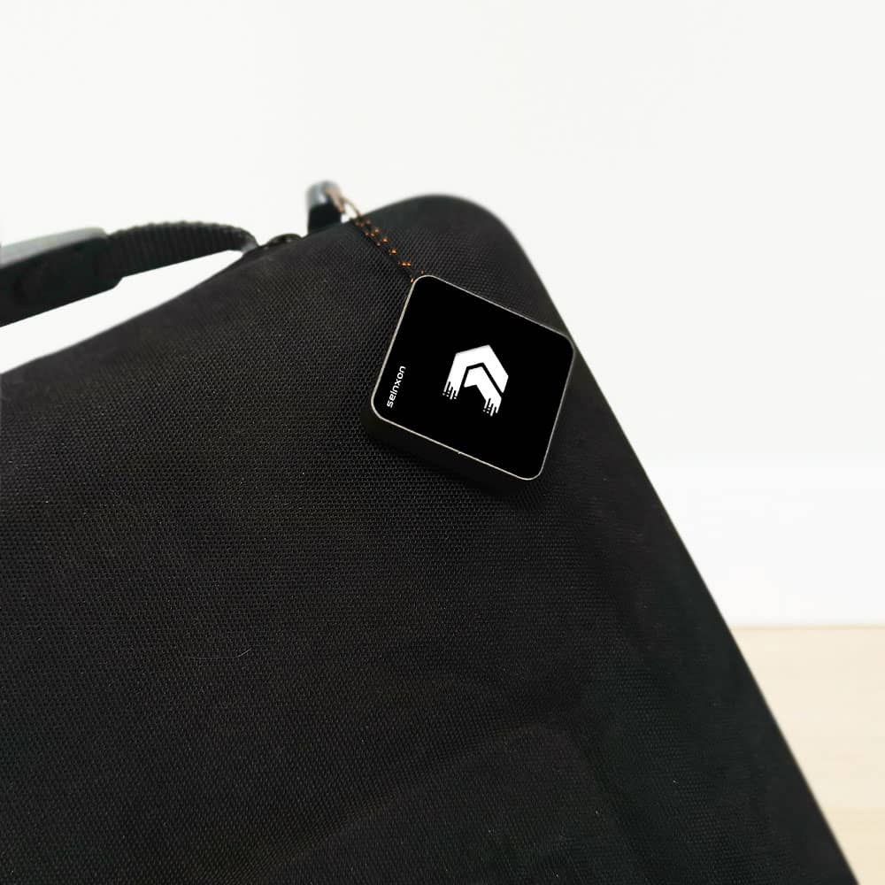 A-black-Seinxon-tracker-with-a-white-house-shaped-logo-attached-to-a-black-fabric-bag-indicating-its-functionality-for-securing-personal-items