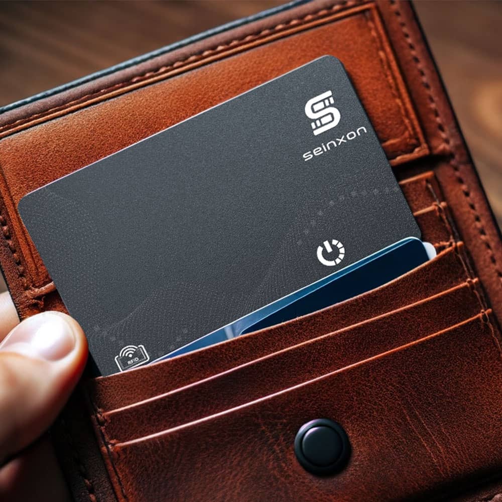 A-person's-hand-is-holding-a-brown-leather-wallet-that-contains-a-Seinxon-locator-card-with-FindMy-functionality-visible-from-the-top-slot-showcasing-the-card's-sleek-design